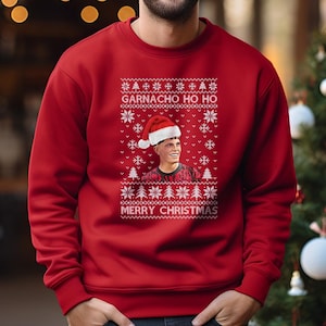 Könnte beinhalten: Ein roter Weihnachtspullover mit dem Text "GARNACHO HO HO" und "MERRY CHRISTMAS" in Weiß. Der Pullover zeigt ein Porträt einer Person mit Weihnachtsmütze. Der Pullover ist ein Rundhals-Stil.