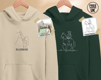 May include: Two beige and green hoodies with a line drawing of a person and a horse on each. The beige hoodie has the text "HADDISH" below the drawing. The green hoodie has a drawing of a person riding a horse. Both hoodies have a photo placeholder with the text "YOUR PHOTO" below it.