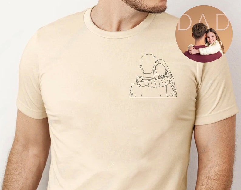 May include: A beige t-shirt with a line drawing of a father and child hugging. The drawing is on the left side of the shirt. The word "DAD" is in the background.