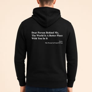 May include: Black hooded sweatshirt featuring the white text: "Dear Person Behind Me, The World Is A Better Place With You In It. Love, The Person In Front Of You". The garment has a hood.