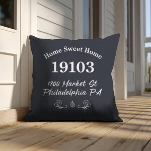 Puede incluir: Un cojín cuadrado azul marino con las palabras "Home Sweet Home" y una dirección en escritura blanca. El cojín está colocado en un porche de madera, ideal para la decoración del hogar.