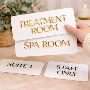 以下が含まれることがあります： TREATMENT ROOMとSPA ROOMと書かれた金色の浮き彫り文字がある白い長方形の看板。その下には、SUITE 1とSTAFF ONLYと書かれた黒い文字の白い長方形の看板が2つあり、すべて角が丸く滑らかな仕上がりになっています。