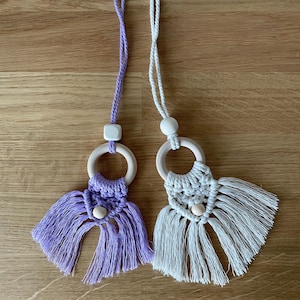 Peut inclure: Deux hochet pour bébé en macramé faits à la main avec des anneaux et des perles en bois. Un hochet est violet et l'autre est blanc.