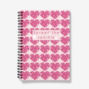 May include: A pink spiral notebook with a pink glitter heart pattern and the text "Spread the sparkle" on the cover.