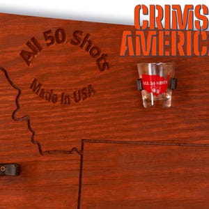 K&ouml;nnte beinhalten: Eine Holzkarte der Vereinigten Staaten mit dem Text "All 50 Shots Made in USA" und "Crimson Americana" darauf gedruckt. Ein Schnapsglas mit dem Text "All 50 Shots" ist an der Karte befestigt.