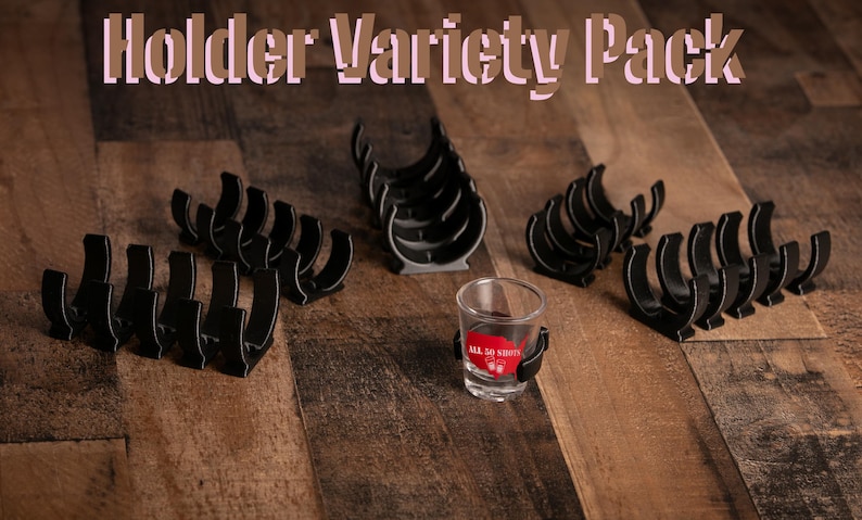 K&ouml;nnte beinhalten: Ein Sortiment an schwarzen Shotglas-Haltern. Die Halter sind aus Kunststoff und so konzipiert, dass sie Shotgl&auml;ser aufrecht halten. Das Sortiment umfasst eine Vielzahl von Formen und Gr&ouml;&szlig;en an Haltern. Der Text "Holder Variety Pack" ist in rosa Buchstaben auf einem Holzgrund geschrieben.