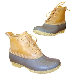 May include: Two tan and gray duck boots with yellow laces. The boots have a rubber bottom and a leather upper. The boots are designed for outdoor activities and are a classic style.