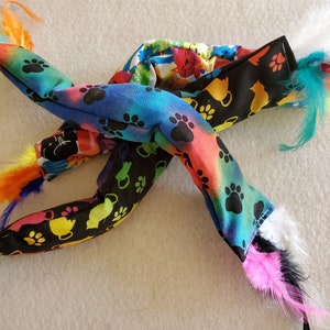 May include: A colorful cat toy with multiple tails made of feathers and fabric. The fabric is printed with paw prints and cats.