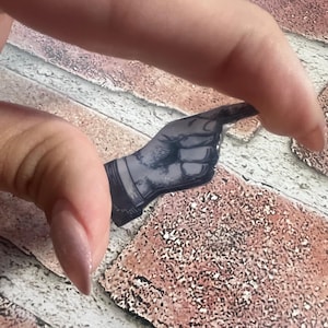 May include: A black and white graphic of a hand pointing, held between fingers. The graphic is a sticker or a small cutout, with the hand's details visible. The background is a brick-patterned surface.