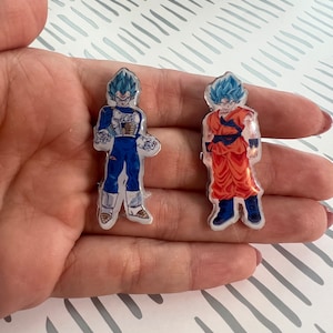 May include: Two anime character figurines, one in blue and one in orange, with blue hair and a white background.