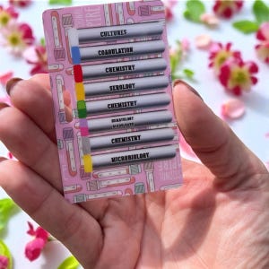 May include: A pink card with a medical theme, featuring the words "Cultures," "Coagulation," "Chemistry," "Serology," "Hematology Blood Bank," and "Microbiology." The card has a pattern of test tubes and is held in a hand.