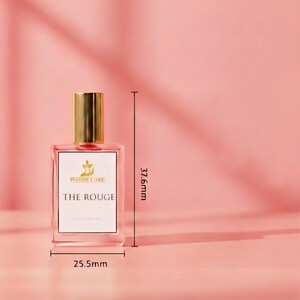 Puede incluir: Un frasco de perfume rectangular con tapa dorada y etiqueta blanca que dice "THE ROUGE". La botella mide 2,55 cm de ancho y 37,6 mm de alto. El fondo es de color rosa liso.