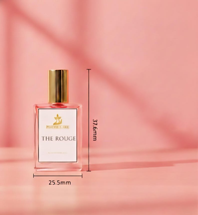 Puede incluir: Un frasco de perfume rectangular con tapa dorada y etiqueta blanca que dice "THE ROUGE". La botella mide 2,55 cm de ancho y 37,6 mm de alto. El fondo es de color rosa liso.