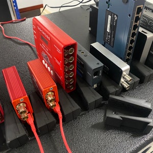 May include: A close-up of a black rack with multiple red and silver electronic devices. The devices have multiple gold connectors and are labelled with text. The rack is on a black surface.