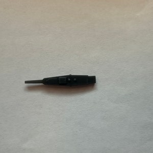 May include: A black plastic tool with a small button and a pointed tip. The tool is used for removing small objects from tight spaces.