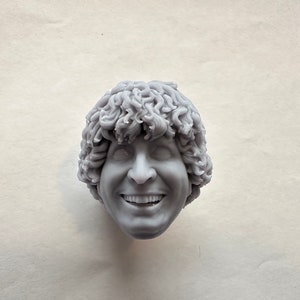 Puede incluir: Busto gris de una persona sonriente con cabello rizado. La escultura tiene un rostro detallado con dientes visibles y ojos cerrados. El busto es un objeto sólido tridimensional.
