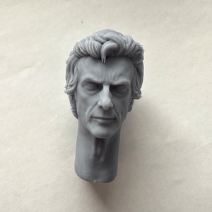 Puede incluir: Busto gris de la cabeza y el cuello de un hombre, con detalles faciales y textura del cabello. La escultura tiene una expresión seria. El busto es una representación detallada.