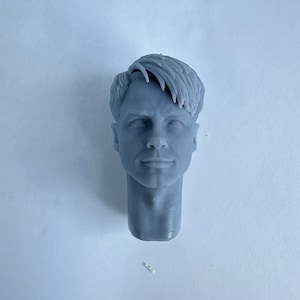 May include: A gray 3D printed head sculpt of a man with short, styled hair. The head is facing forward with a neutral expression.