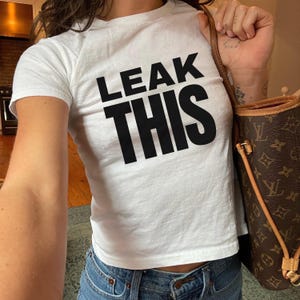 Könnte beinhalten: Weißes, bauchfreies T-Shirt mit schwarzem Text "LEAK THIS".