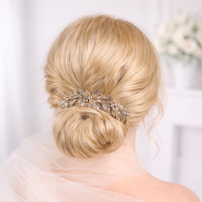 the back view of a woman's blonde hair with a decorative hair accessory, possibly a veil or headpiece, styled in a bun.