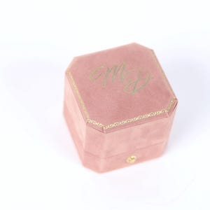 A pink velvet ring box with the initials 'M.D.' embossed on it.