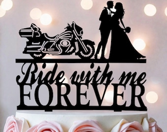 May include: A black cake topper featuring a silhouette of a motorcycle next to a couple standing together. The text "Ride with me FOREVER" is displayed in a decorative script and block font below the figures, all set on a flat base.