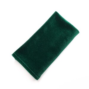 May include: A rectangular, emerald green velvet napkin, folded neatly. The fabric has a soft, plush texture, and the edges are precisely sewn. The napkin is set against a plain white background, highlighting its rich color and elegant simplicity.