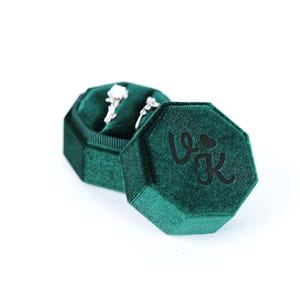 A green velvet jewelry box containing two diamond earrings.