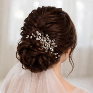 A woman's hair is styled in an elaborate updo, adorned with a decorative hair accessory featuring a floral and crystal embellishment.