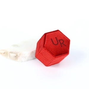 A red hexagonal object with the letters "UR" printed on it, placed on a white surface.