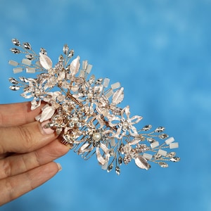 A hand holding a decorative piece of jewelry against a blue background.