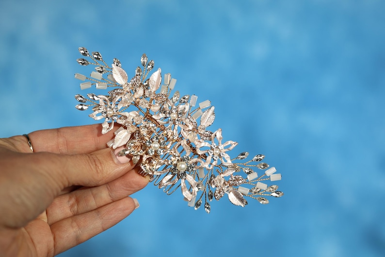 A hand holding a decorative piece of jewelry against a blue background.
