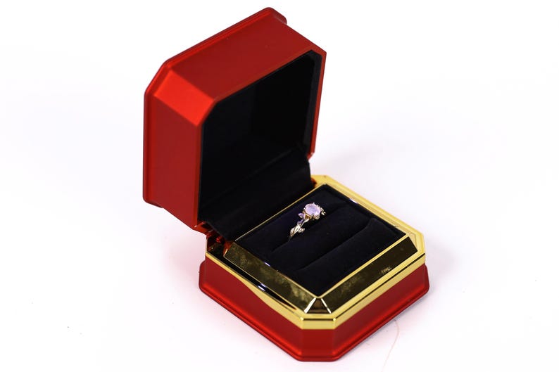 A red and gold jewelry box containing a ring, placed on a white background.