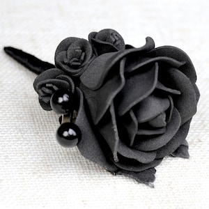 May include: A black fabric rose with a stem and two black beads. The rose is made of fabric and has a realistic look.