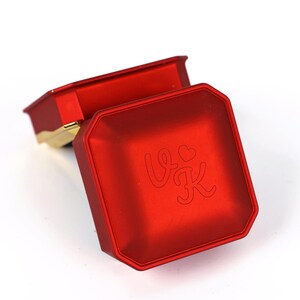 A red metal box with a heart and letter "V" engraved on it.