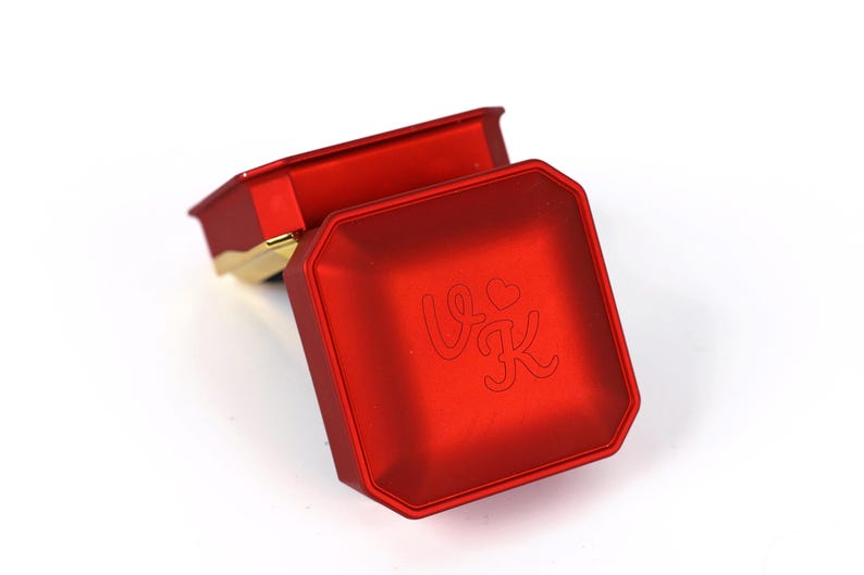 A red metal box with a heart and letter "V" engraved on it.