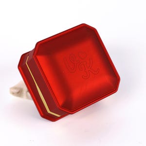 A red metal box with a gold border, featuring a logo or text on its surface.