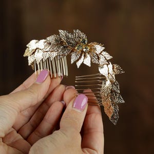 A close-up image of a person's hands holding a decorative gold hair accessory with leaves and gemstones.
