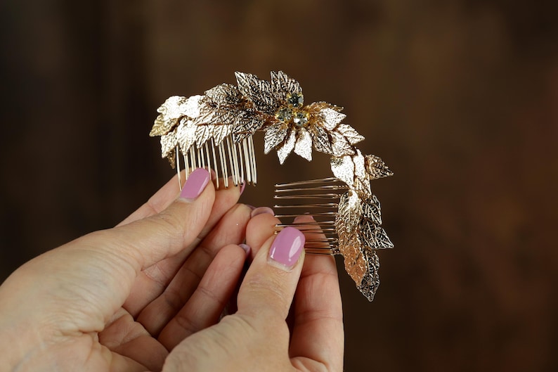 A close-up image of a person's hands holding a decorative gold hair accessory with leaves and gemstones.