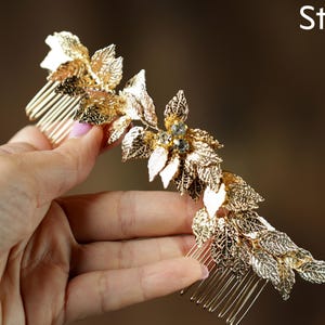 A hand holding a decorative gold hair accessory with leaves and gemstones.