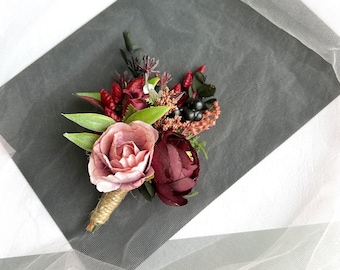 May include: A small bouquet of artificial flowers in shades of pink and burgundy. The bouquet includes roses, berries, and greenery. It is tied with twine and would be suitable for a wedding or other special occasion.