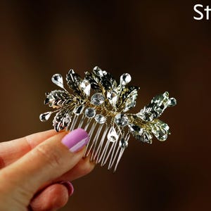A hand holding a decorative hair accessory with a floral design and sparkling crystal elements.