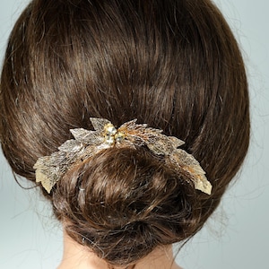 the back of a person's head with a decorative hair accessory, featuring a combination of leaves and flowers.