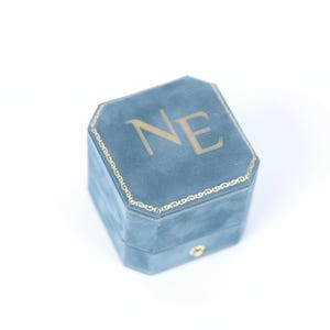 A blue velvet ring box with the letters 'NE' printed on it.