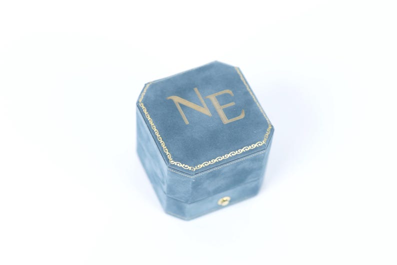 A blue velvet ring box with the letters 'NE' printed on it.