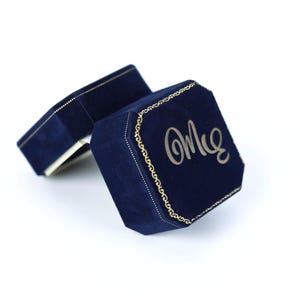 a pair of navy blue velvet jewelry boxes with gold accents, one of which has the word "Om" written on it.