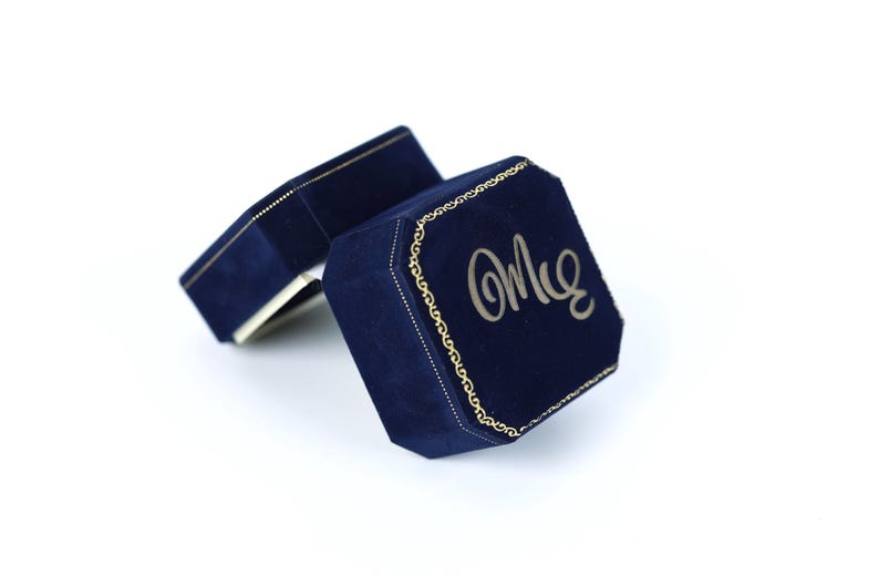a pair of navy blue velvet jewelry boxes with gold accents, one of which has the word "Om" written on it.