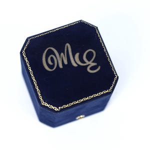 A blue velvet jewelry box with the word "Omle" embossed on it.
