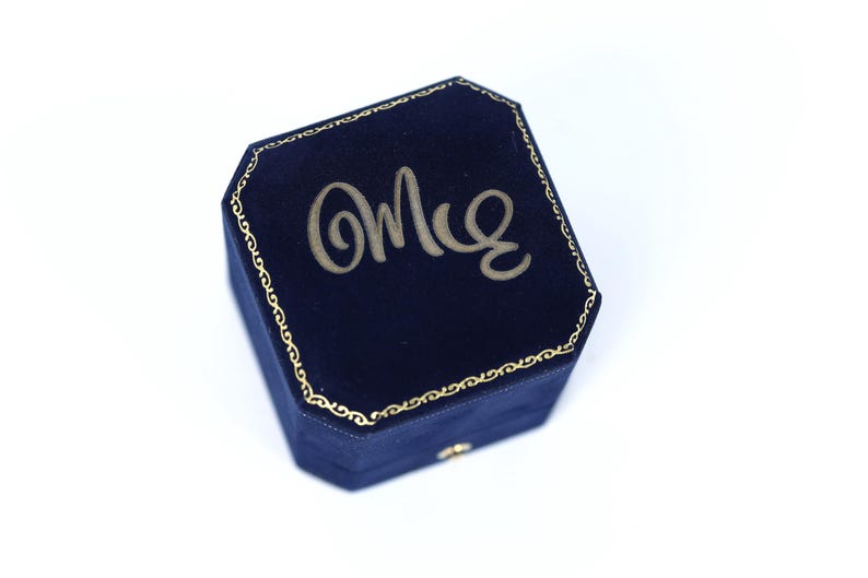 A blue velvet jewelry box with the word "Omle" embossed on it.