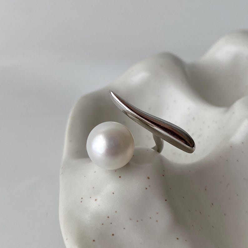 May include: A silver ring featuring a white pearl and a curved silver band.